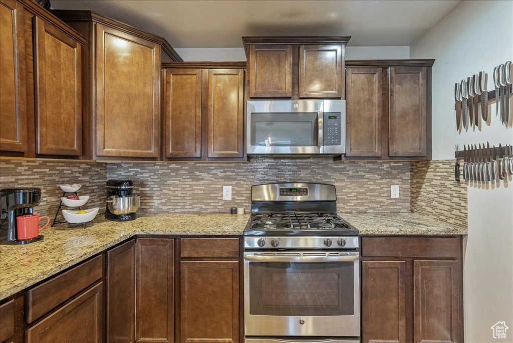 Kitchen with light stone counters, decorative backsplash, and stainless steel appliances