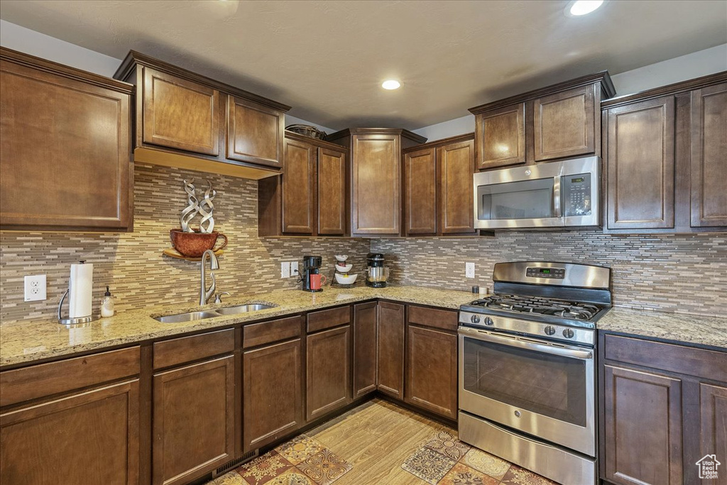 Kitchen featuring stainless steel appliances, sink, backsplash, and light stone counters