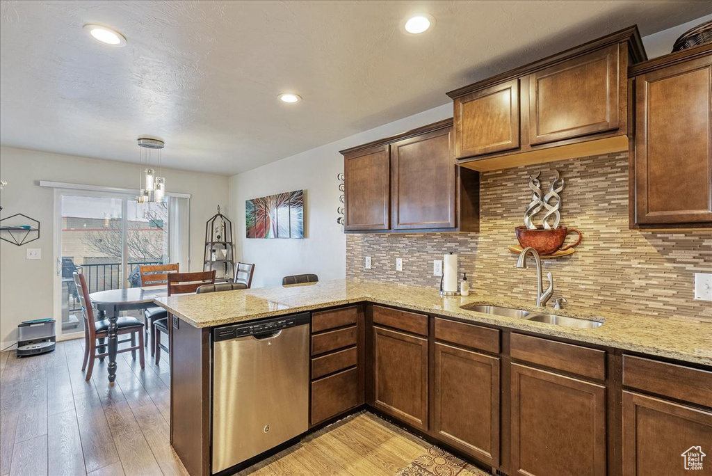 Kitchen featuring sink, hanging light fixtures, light hardwood / wood-style flooring, dishwasher, and kitchen peninsula