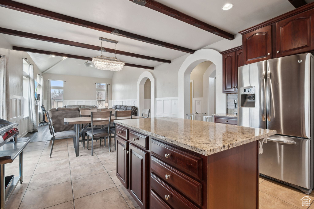 Kitchen with stainless steel fridge with ice dispenser, hanging light fixtures, light tile patterned floors, a kitchen island, and light stone countertops