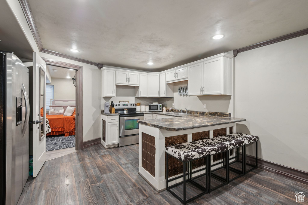 Kitchen with a kitchen bar, appliances with stainless steel finishes, dark hardwood / wood-style floors, kitchen peninsula, and white cabinets