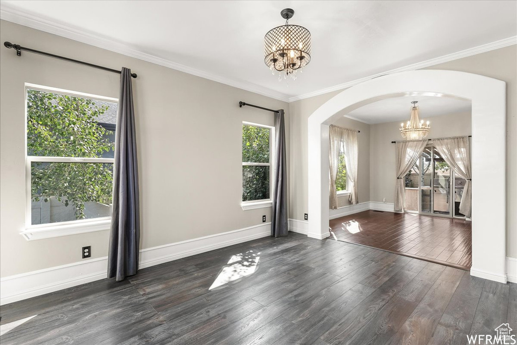 Empty room with dark wood-type flooring, ornamental molding, and a notable chandelier