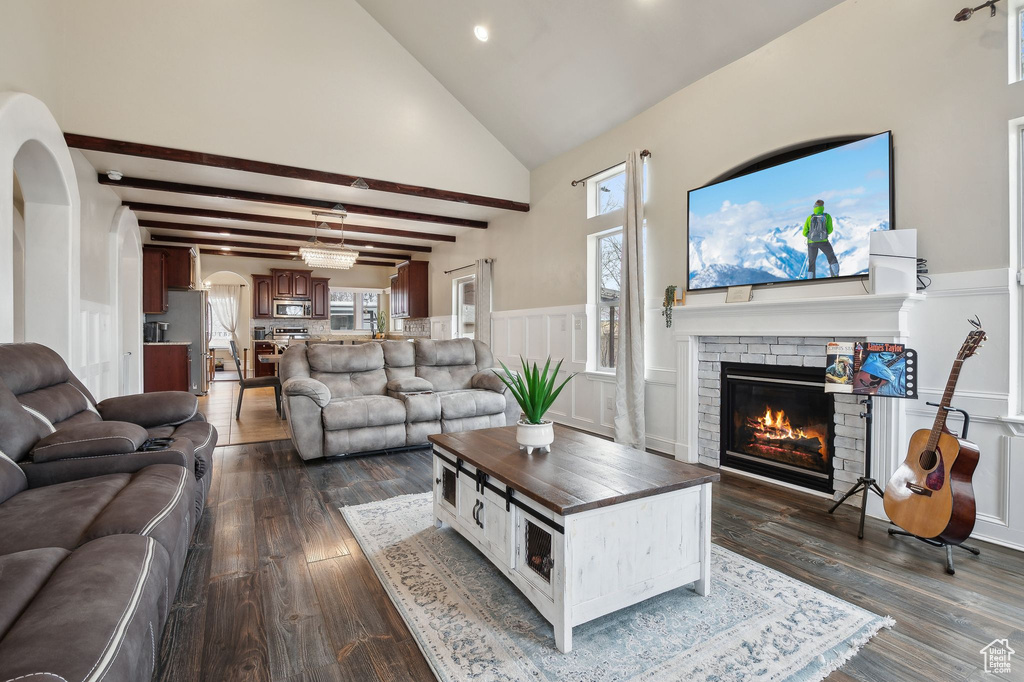 Living room with dark wood-type flooring, high vaulted ceiling, a brick fireplace, and beamed ceiling