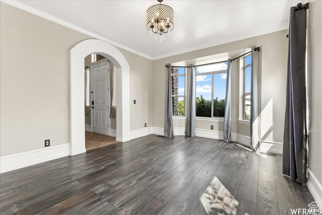 Empty room with ornamental molding, dark hardwood / wood-style floors, and a chandelier