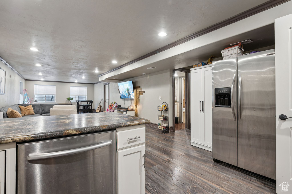 Kitchen with white cabinetry, stainless steel appliances, dark hardwood / wood-style floors, ornamental molding, and dark stone counters