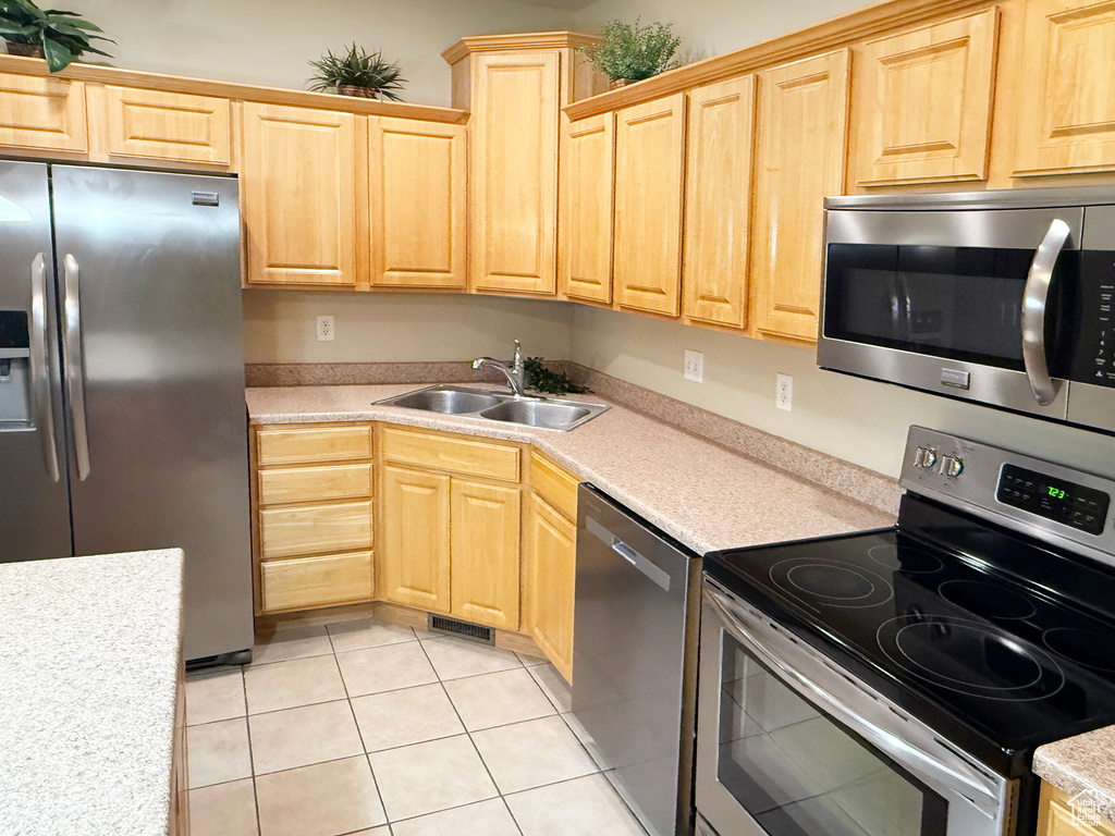 Kitchen with appliances with stainless steel finishes, sink, light tile patterned floors, and light brown cabinets