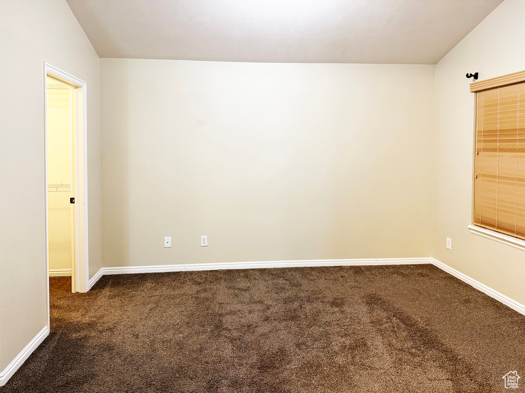 Spare room featuring vaulted ceiling and dark colored carpet