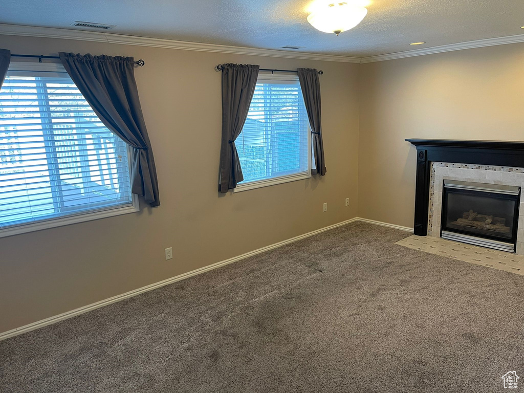 Unfurnished living room with ornamental molding, carpet flooring, a tile fireplace, and a textured ceiling