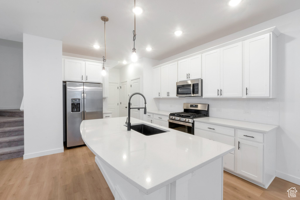 Kitchen with sink, appliances with stainless steel finishes, hanging light fixtures, an island with sink, and white cabinets