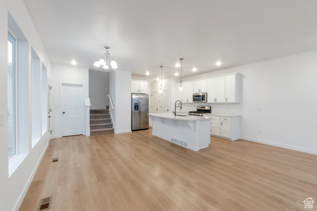 Kitchen with white cabinetry, sink, hanging light fixtures, a kitchen island with sink, and stainless steel appliances
