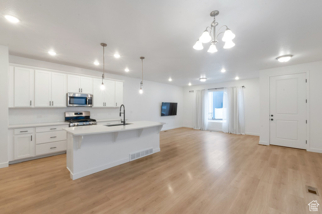 Kitchen featuring appliances with stainless steel finishes, decorative light fixtures, a kitchen island with sink, and white cabinets