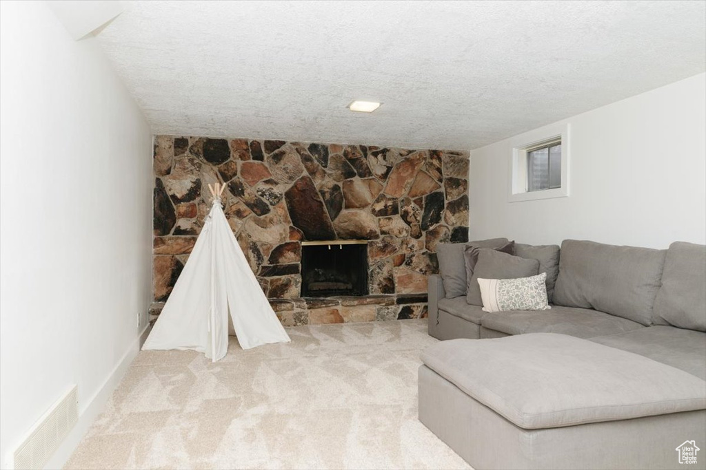 Carpeted living room featuring a stone fireplace and a textured ceiling