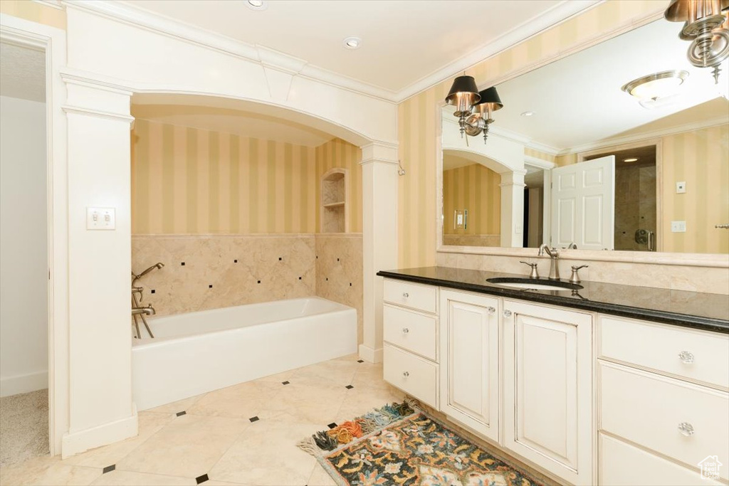 Bathroom featuring decorative columns, crown molding, vanity, and a tub to relax in