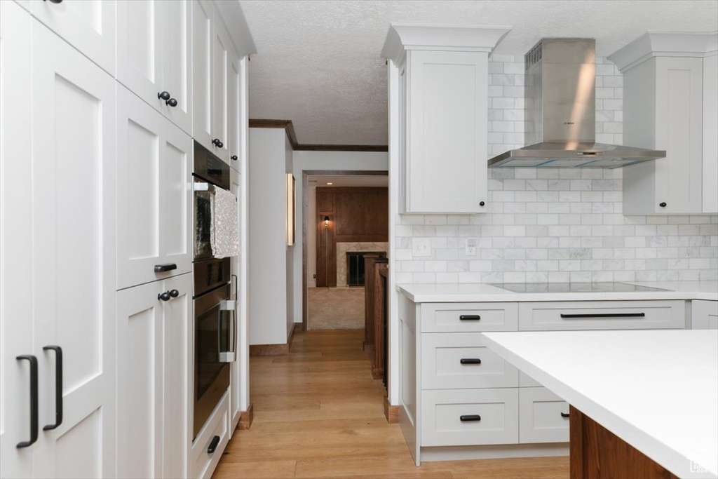 Kitchen with white cabinetry, backsplash, ornamental molding, black electric stovetop, and wall chimney exhaust hood