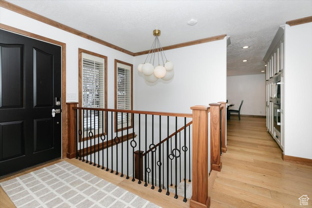 Foyer entrance with crown molding, a notable chandelier, a textured ceiling, and light hardwood / wood-style flooring