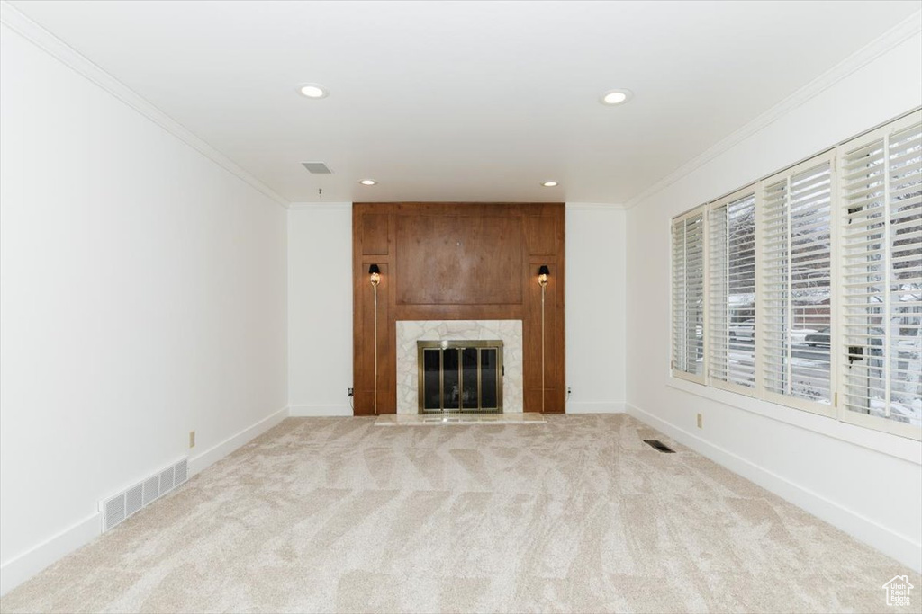 Unfurnished living room featuring crown molding, light colored carpet, and a premium fireplace