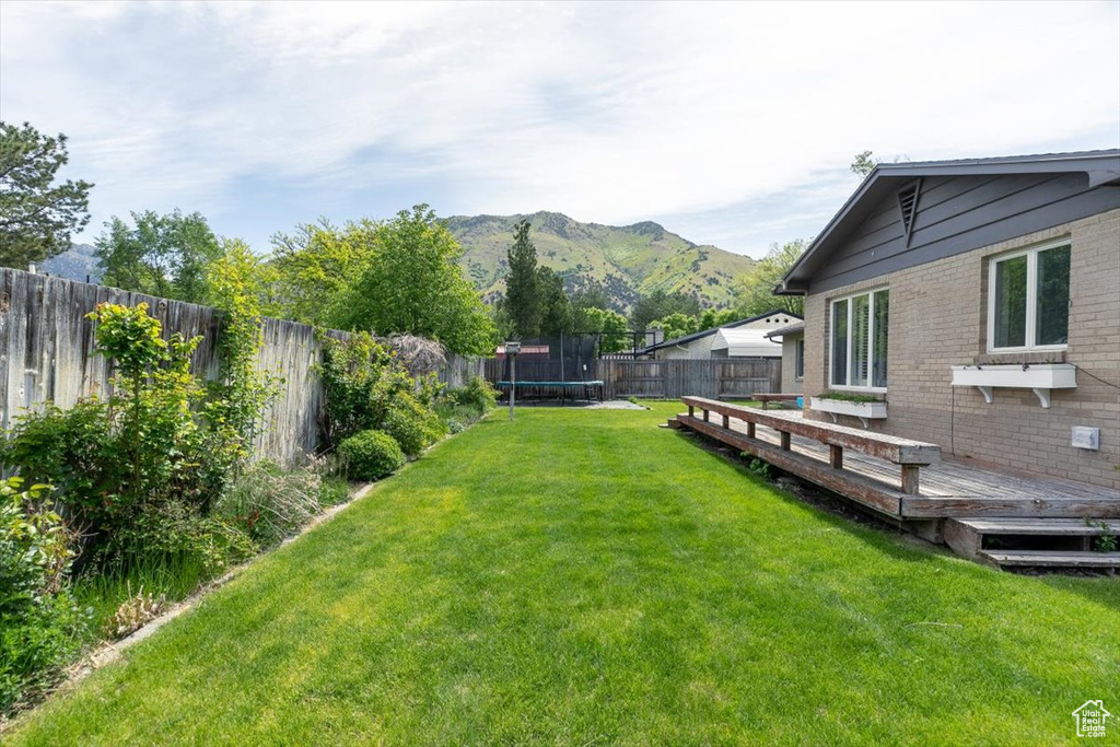 View of yard with a trampoline and a deck with mountain view