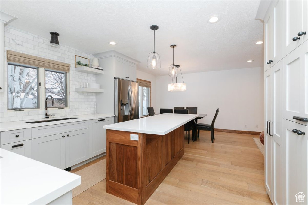 Kitchen featuring sink, stainless steel fridge with ice dispenser, a kitchen island, and white cabinets