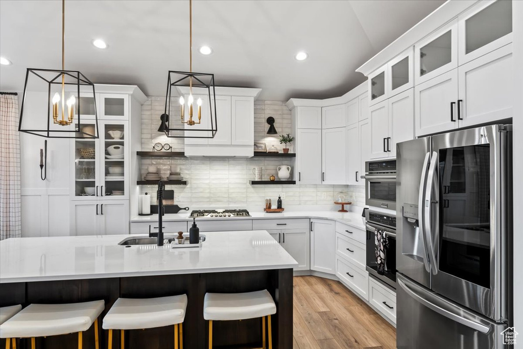 Kitchen featuring decorative light fixtures, tasteful backsplash, white cabinets, stainless steel appliances, and a center island with sink