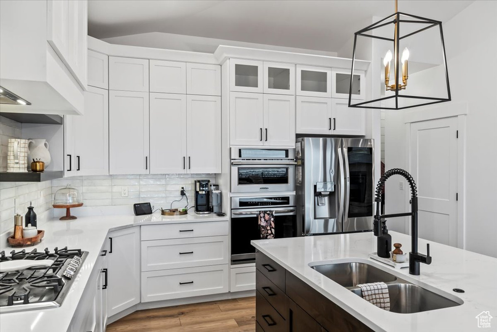 Kitchen featuring pendant lighting, white cabinetry, sink, backsplash, and stainless steel appliances