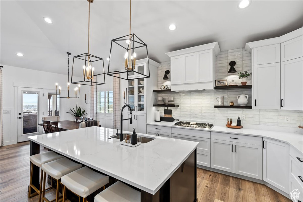 Kitchen with hanging light fixtures, an island with sink, sink, and white cabinets