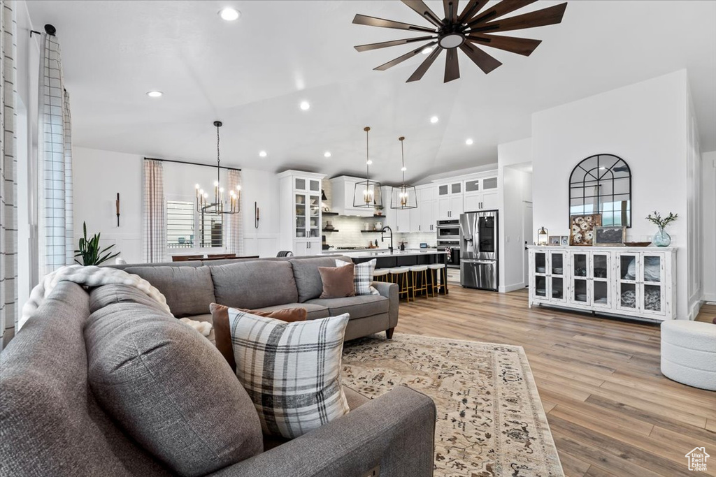 Living room with vaulted ceiling, a healthy amount of sunlight, ceiling fan with notable chandelier, and light wood-type flooring