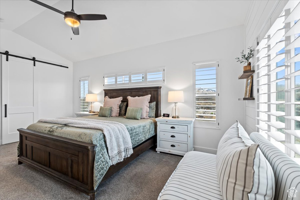 Bedroom with lofted ceiling, a barn door, ceiling fan, and dark colored carpet