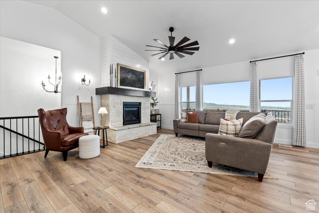 Living room featuring vaulted ceiling, a stone fireplace, ceiling fan with notable chandelier, and light wood-type flooring