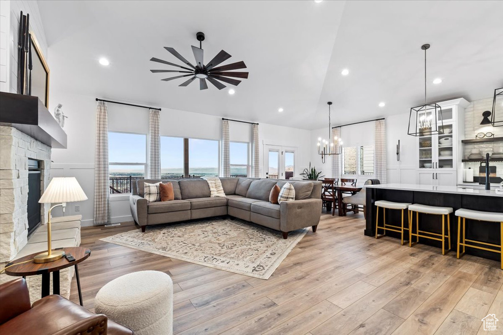 Living room featuring lofted ceiling, a stone fireplace, ceiling fan with notable chandelier, and light wood-type flooring