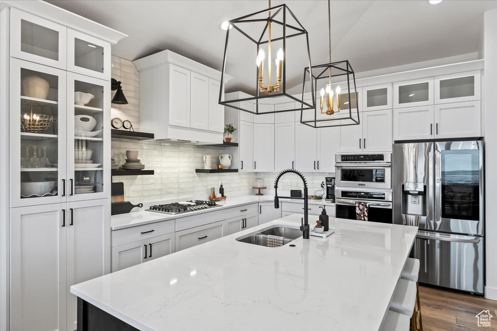 Kitchen with sink, appliances with stainless steel finishes, pendant lighting, decorative backsplash, and white cabinets