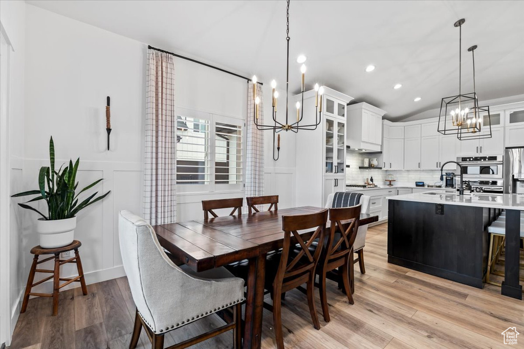 Dining area featuring an inviting chandelier, sink, light hardwood / wood-style flooring, and lofted ceiling