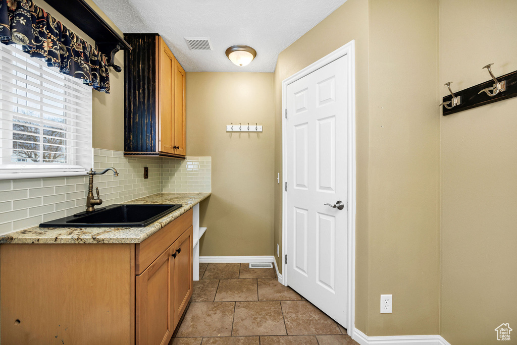 Kitchen with tasteful backsplash, sink, light stone counters, and a textured ceiling