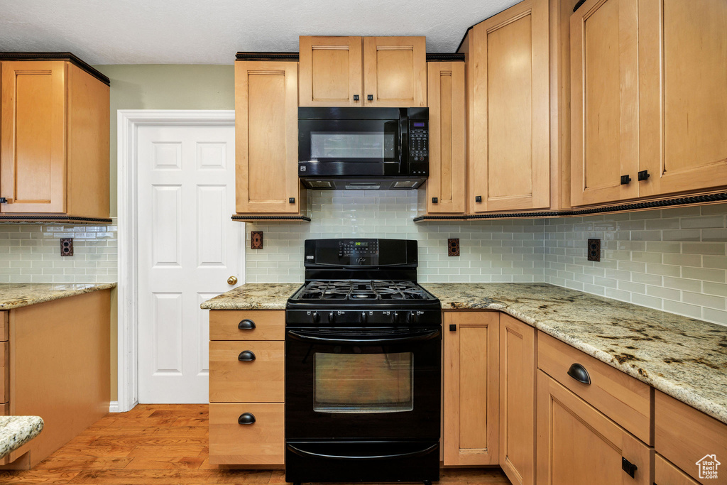 Kitchen featuring light stone counters, light hardwood / wood-style floors, decorative backsplash, and black appliances