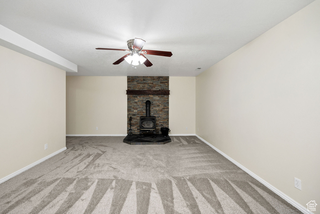 Unfurnished living room with ceiling fan, light carpet, and a wood stove