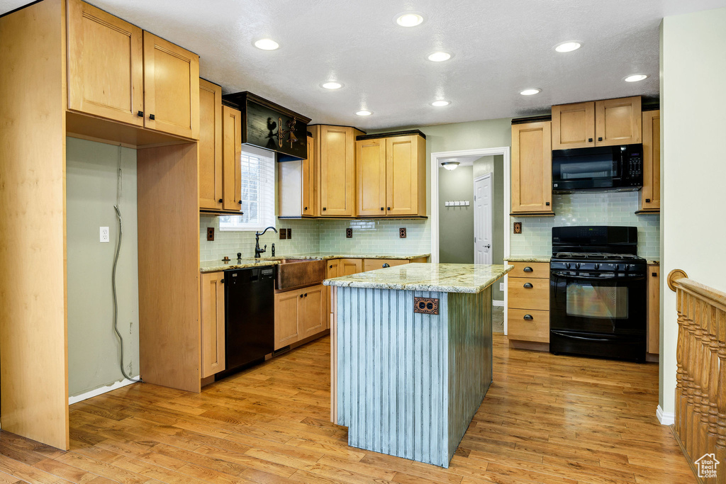 Kitchen with sink, a center island, light stone counters, light hardwood / wood-style floors, and black appliances