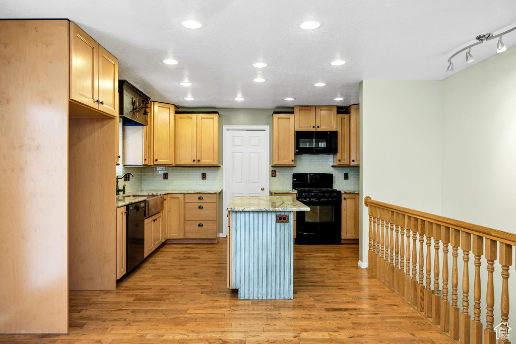 Kitchen with light wood-type flooring, a kitchen island, light stone countertops, decorative backsplash, and black appliances