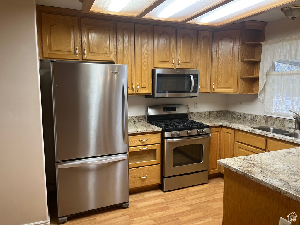 Kitchen featuring light stone counters, open shelves, a sink, light wood-style flooring, and appliances with stainless steel finishes