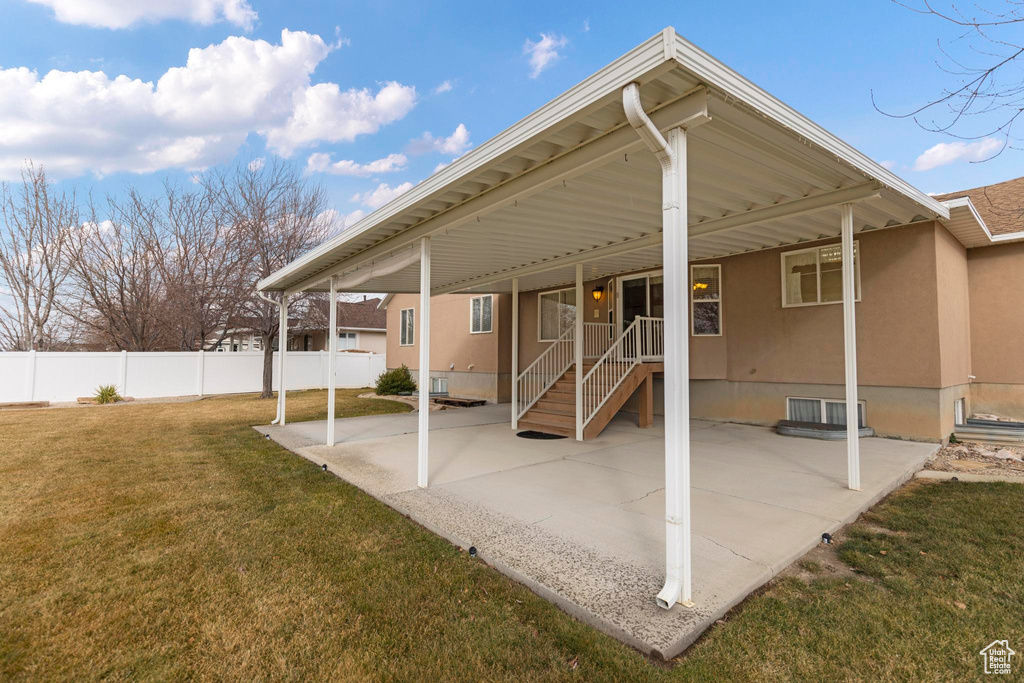 Rear view of property featuring stucco siding, a patio area, a lawn, and fence