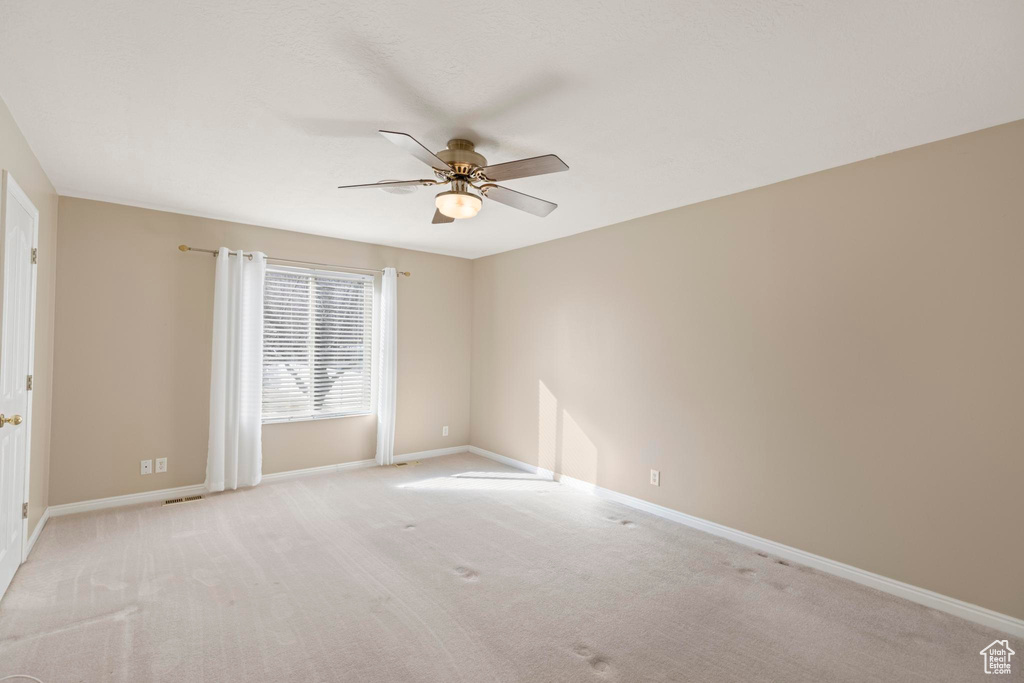 Empty room featuring a ceiling fan, baseboards, and light carpet