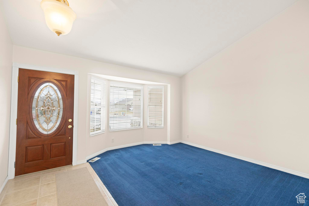 Foyer entrance with light colored carpet, baseboards, vaulted ceiling, and visible vents