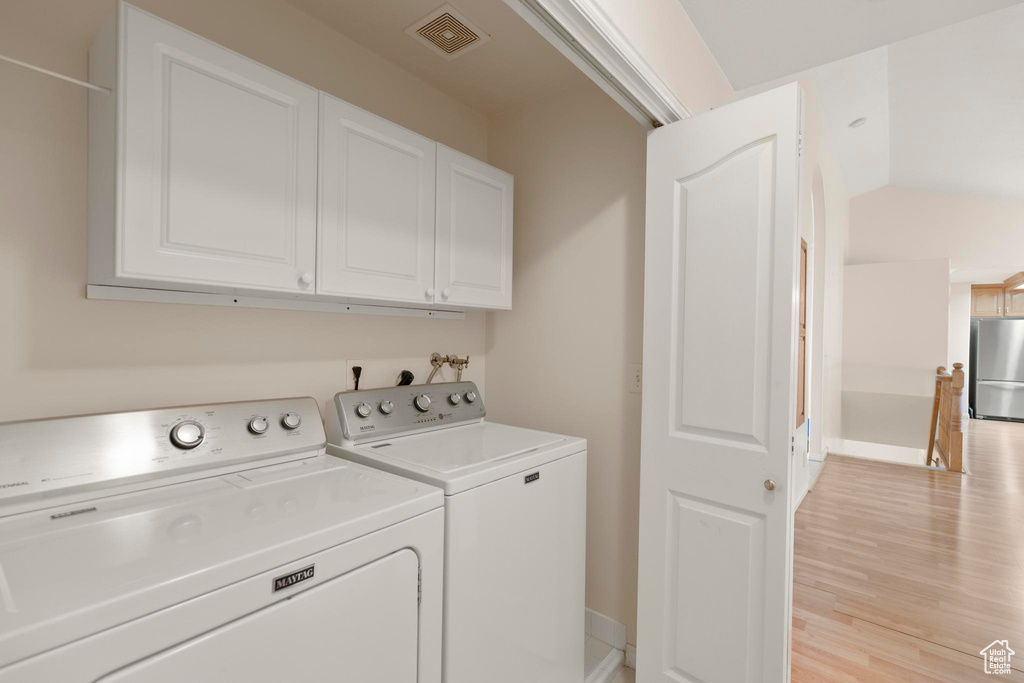 Laundry area with visible vents, washing machine and clothes dryer, baseboards, cabinet space, and light wood-style flooring