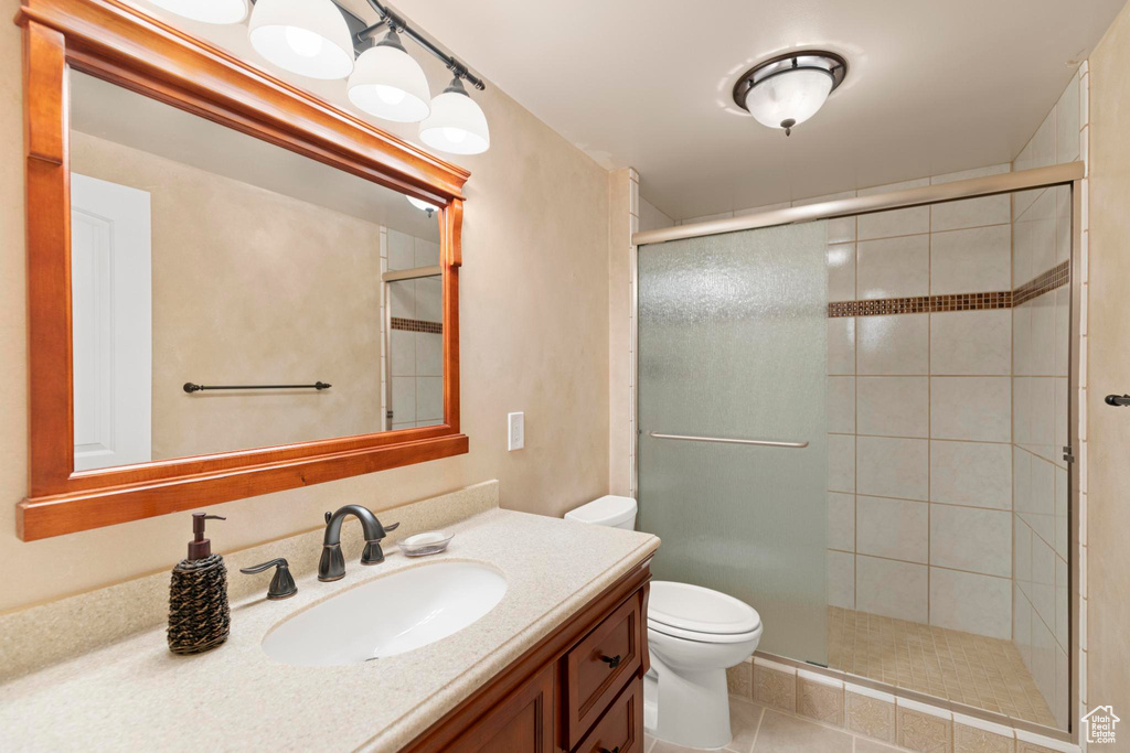 Bathroom featuring toilet, vanity, tile patterned floors, and a stall shower