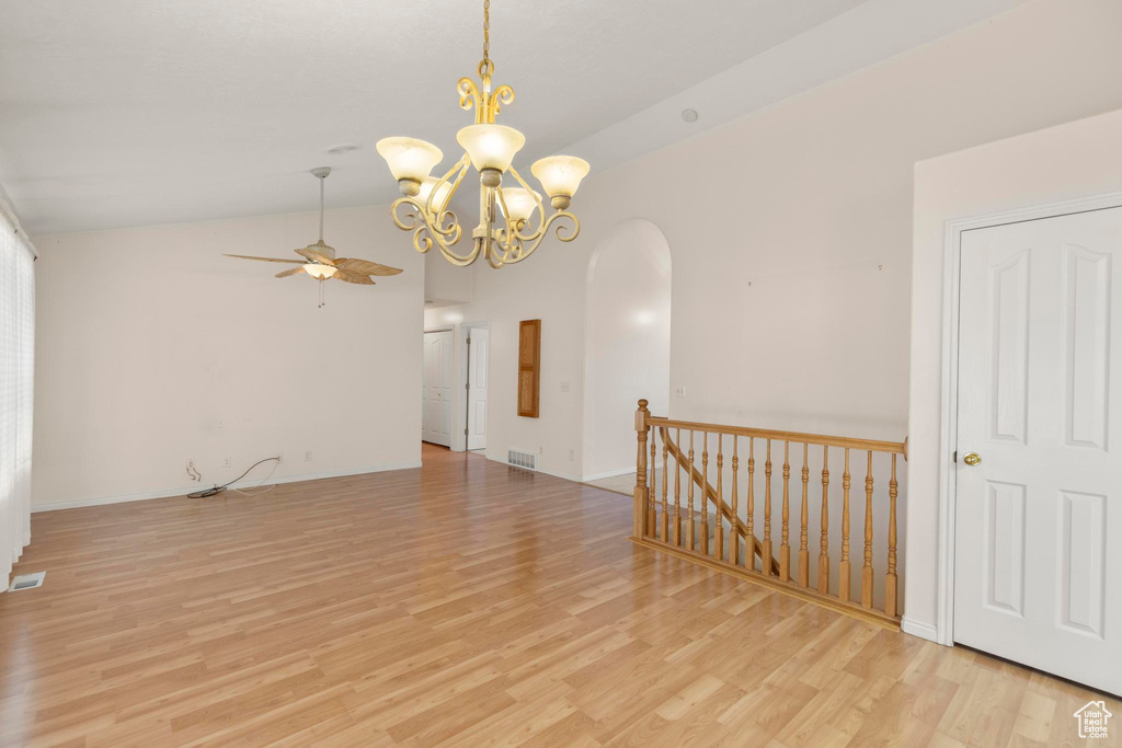 Unfurnished room with light wood finished floors, arched walkways, visible vents, ceiling fan with notable chandelier, and lofted ceiling