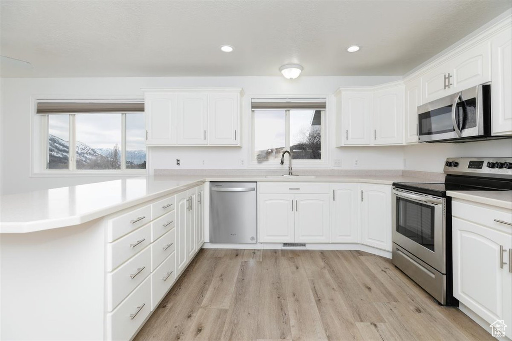 Kitchen featuring stainless steel appliances, sink, white cabinets, and light hardwood / wood-style floors