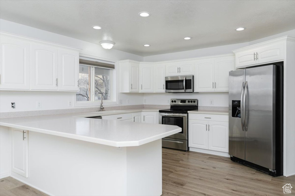 Kitchen featuring sink, white cabinets, kitchen peninsula, stainless steel appliances, and light hardwood / wood-style flooring