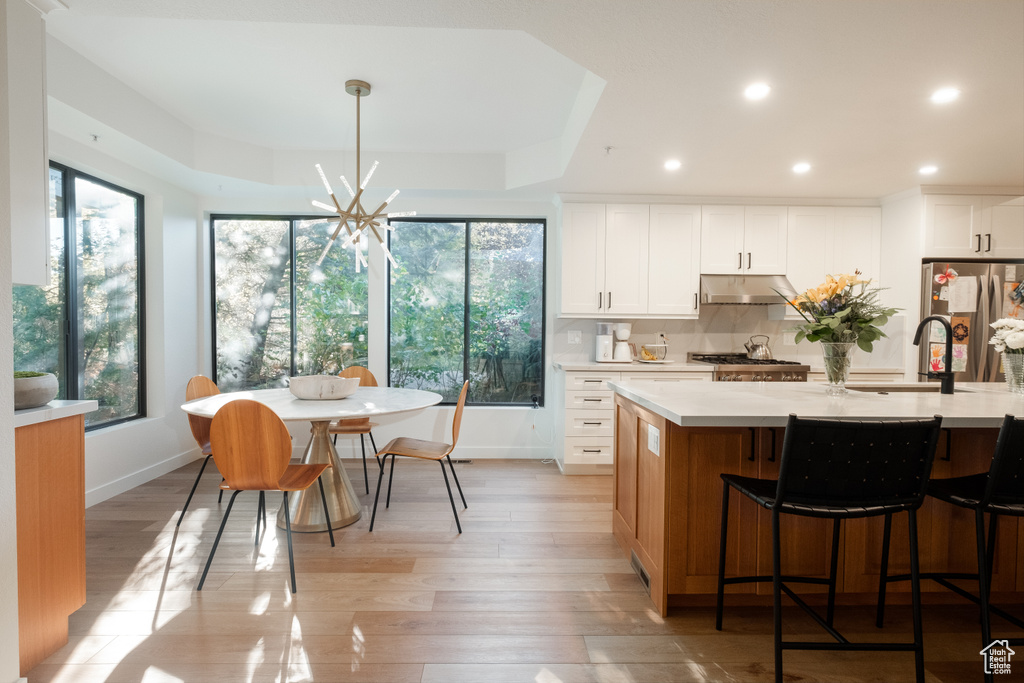 Kitchen featuring stainless steel fridge, an island with sink, white cabinets, decorative light fixtures, and light wood-type flooring