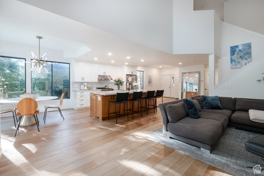 Living room with sink, a chandelier, light wood-type flooring, a tray ceiling, and a towering ceiling
