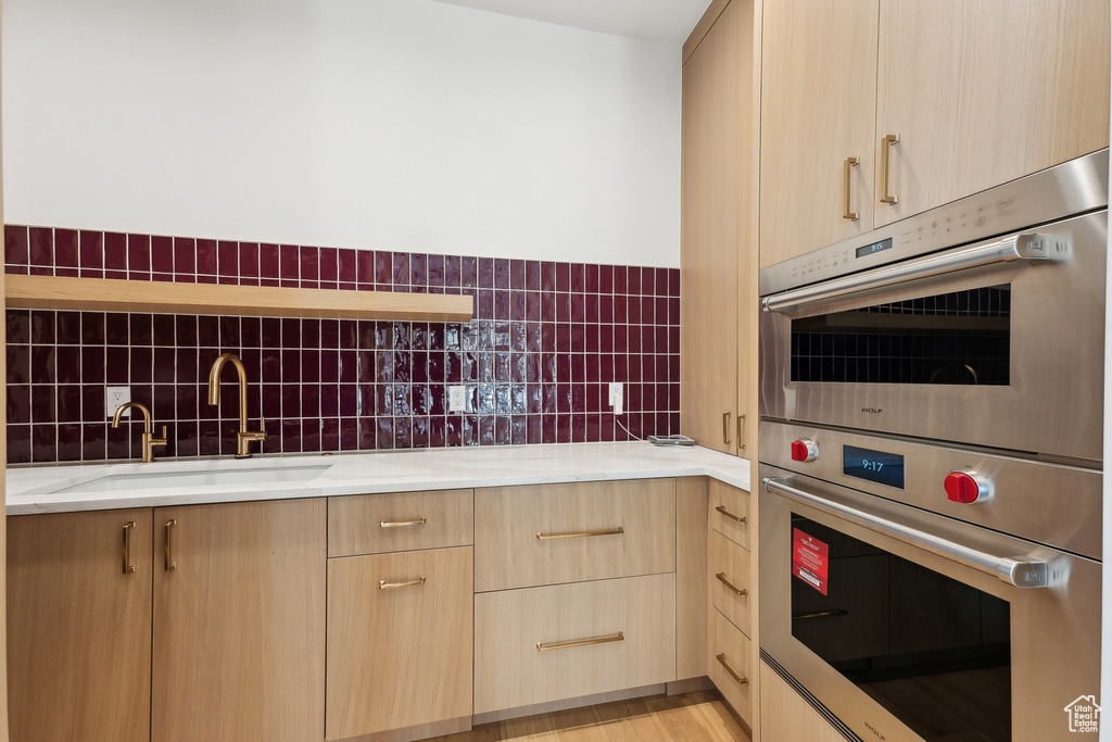 Kitchen with light brown cabinets, double oven, a sink, light stone countertops, and modern cabinets