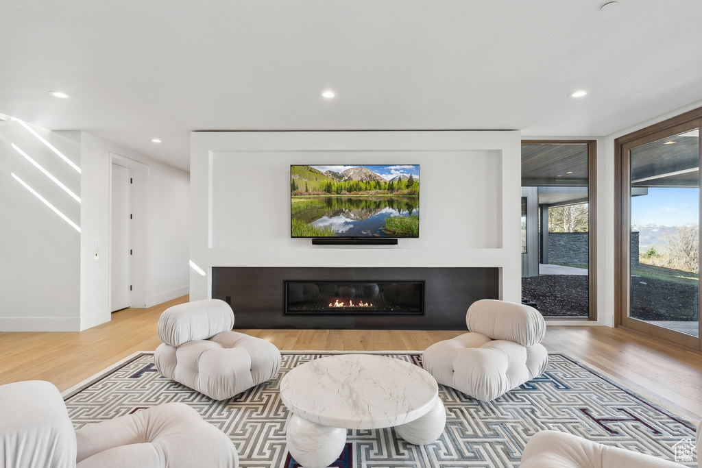 Living room featuring wood finished floors, recessed lighting, a glass covered fireplace, and baseboards