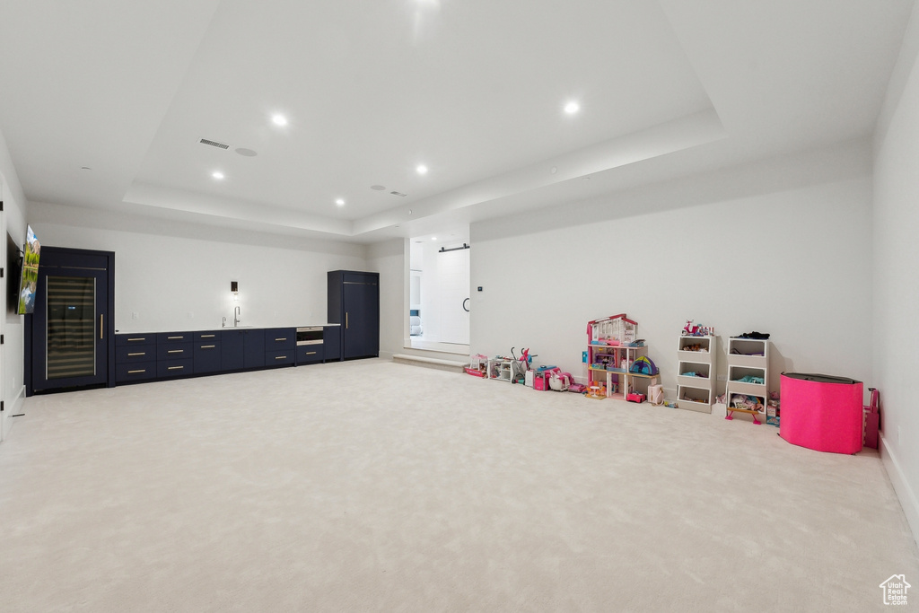Recreation room with a tray ceiling, light colored carpet, wet bar, baseboards, and recessed lighting